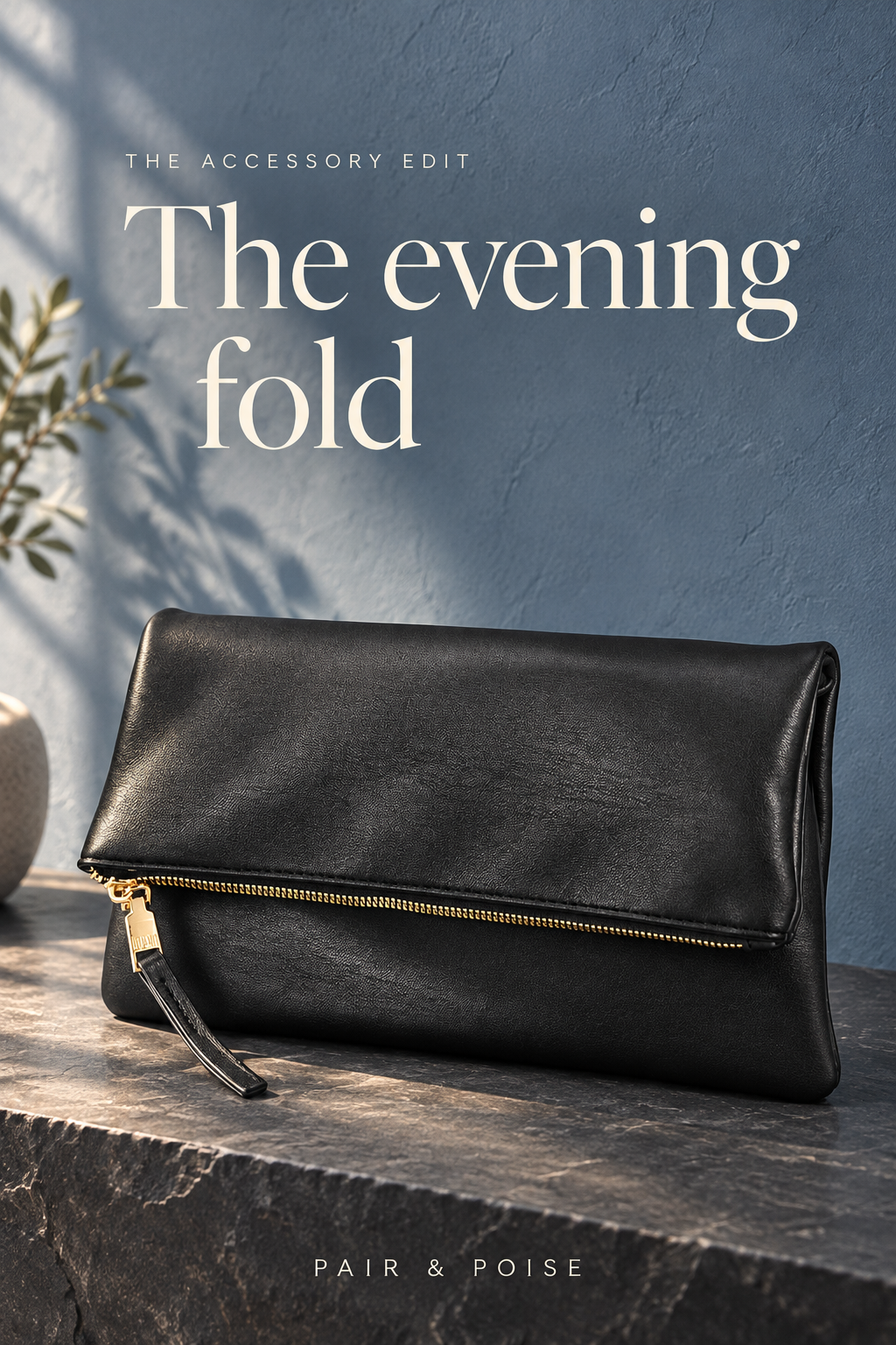 Black foldover clutch with gold zipper and long flat black pull resting on a slate console against a blue plaster wall in natural window light.