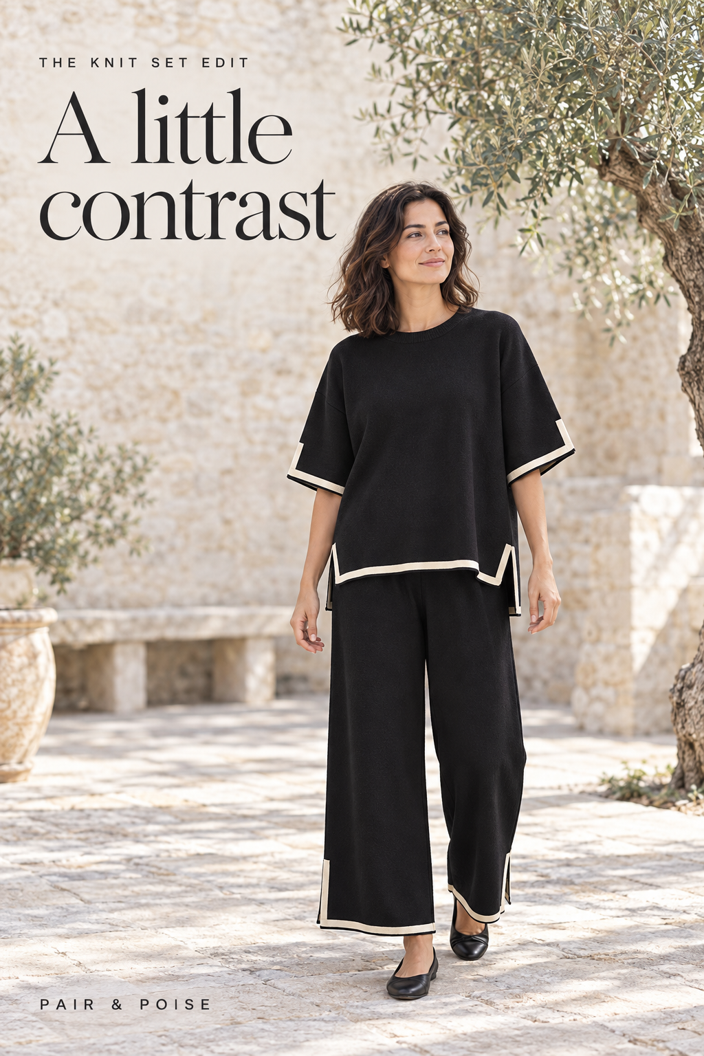 Fictional adult wearing a black short-sleeve knit top and wide-leg pants with narrow cream contrast trim in a sunlit stone courtyard.