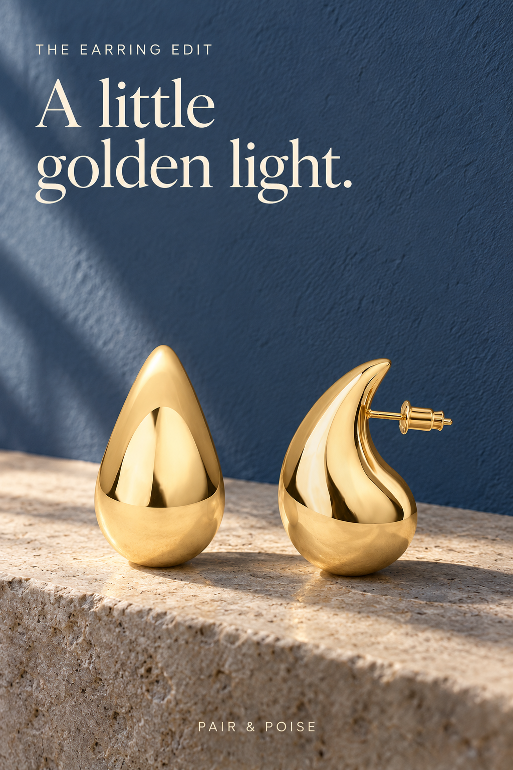 Pair of polished yellow-gold teardrop earrings on a pale stone ledge against dusty-blue plaster; front and side views show rounded bodies and a post with push-back fastening.